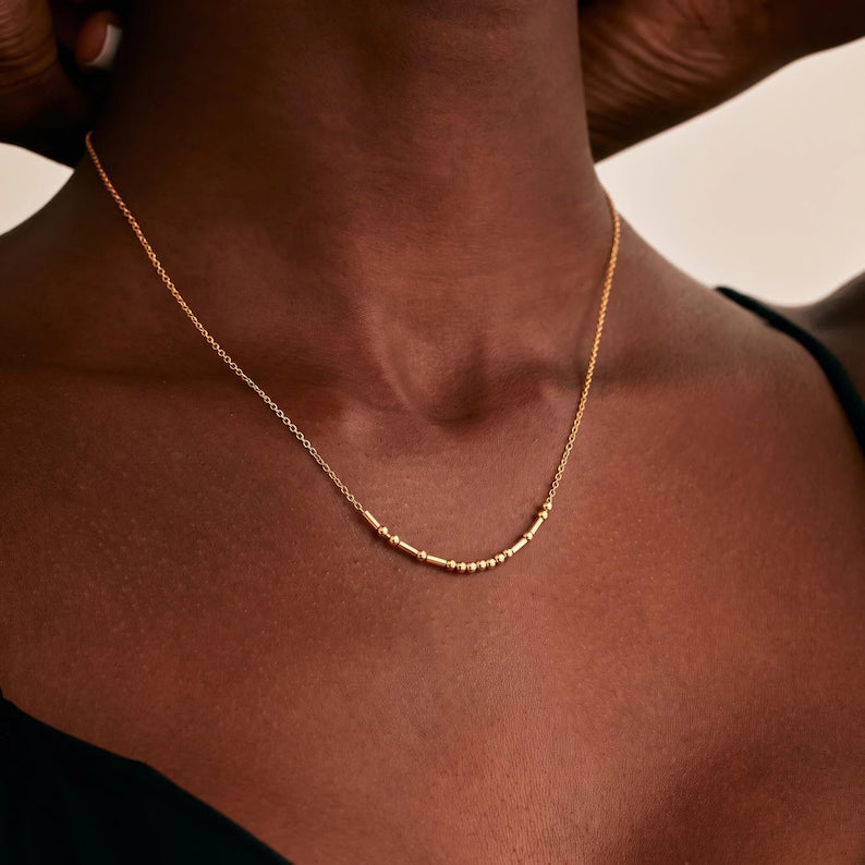 Dainty gold tone Morse code necklace with a hidden message in beads and bars worn on a woman's neck