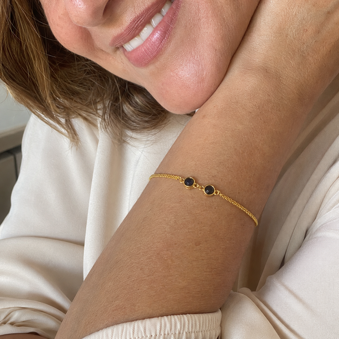 Smiling woman resting her chin on her hand, wearing a gold double photo bracelet
