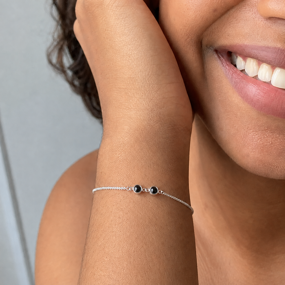 Smiling woman wearing a delicate silver custom photo bracelet with two projection stones