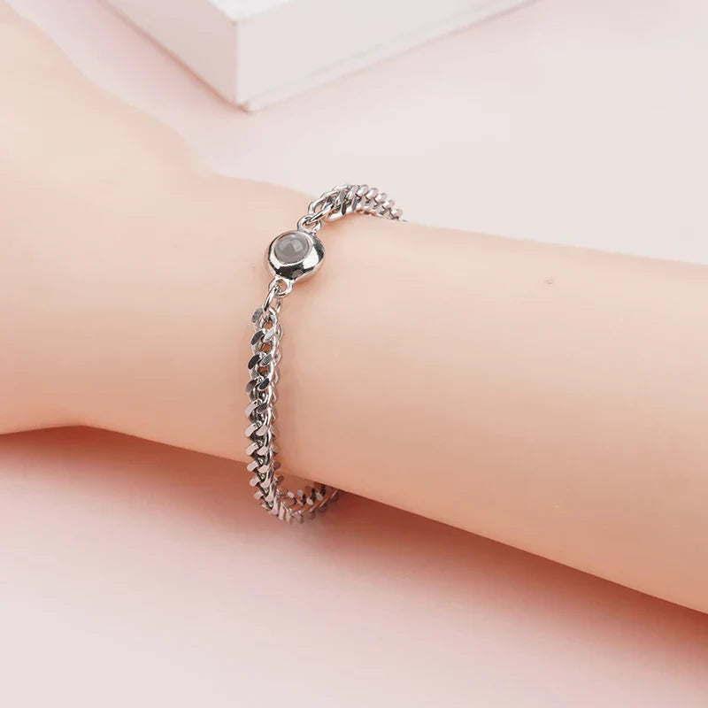 Silver chain bracelet with a round photo stone worn on a wrist against a pink background