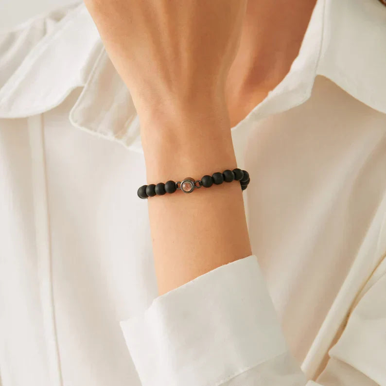 Matte black bead bracelet with a small photo stone worn on a woman's wrist against a white shirt