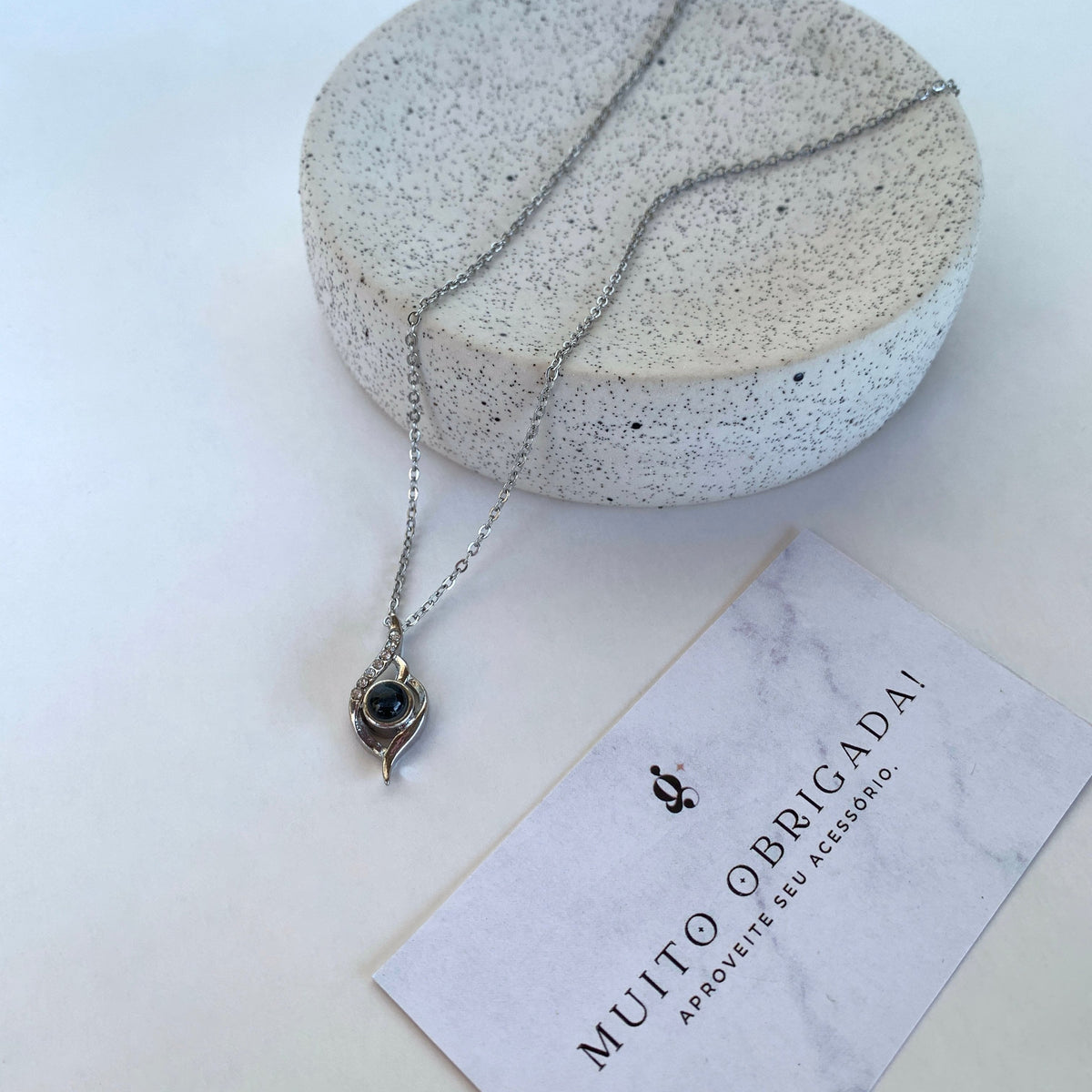 GemShopのサンキューカードの横、石の小皿に置いた写真入りシルバーのしずくペンダントネックレス