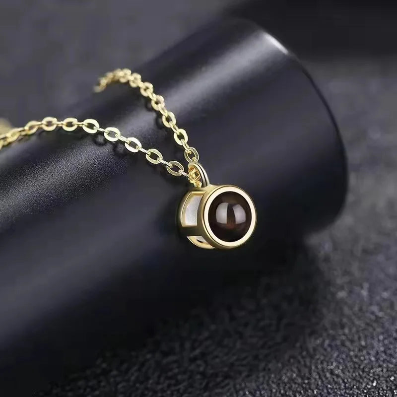 Gold necklace with picture inside, round pendant with a dark photo stone resting on a black cylinder