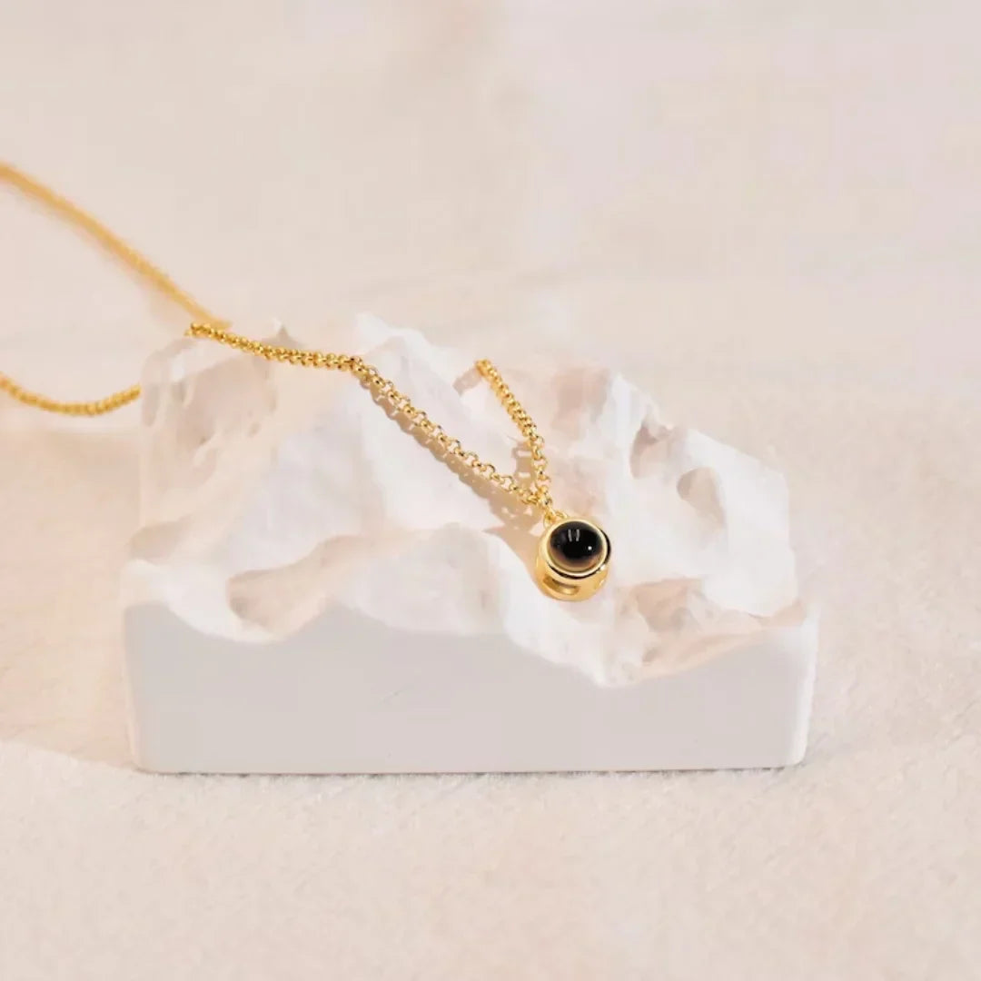 Gold photo projection necklace with a small round black stone draped over a white sculpted block