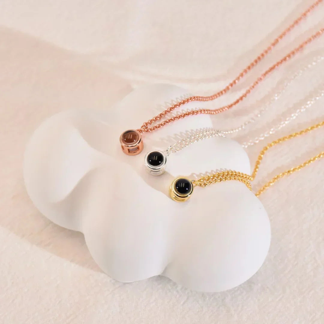 Three photo projection necklaces in rose gold, silver and gold with black stones on a white cloud stand