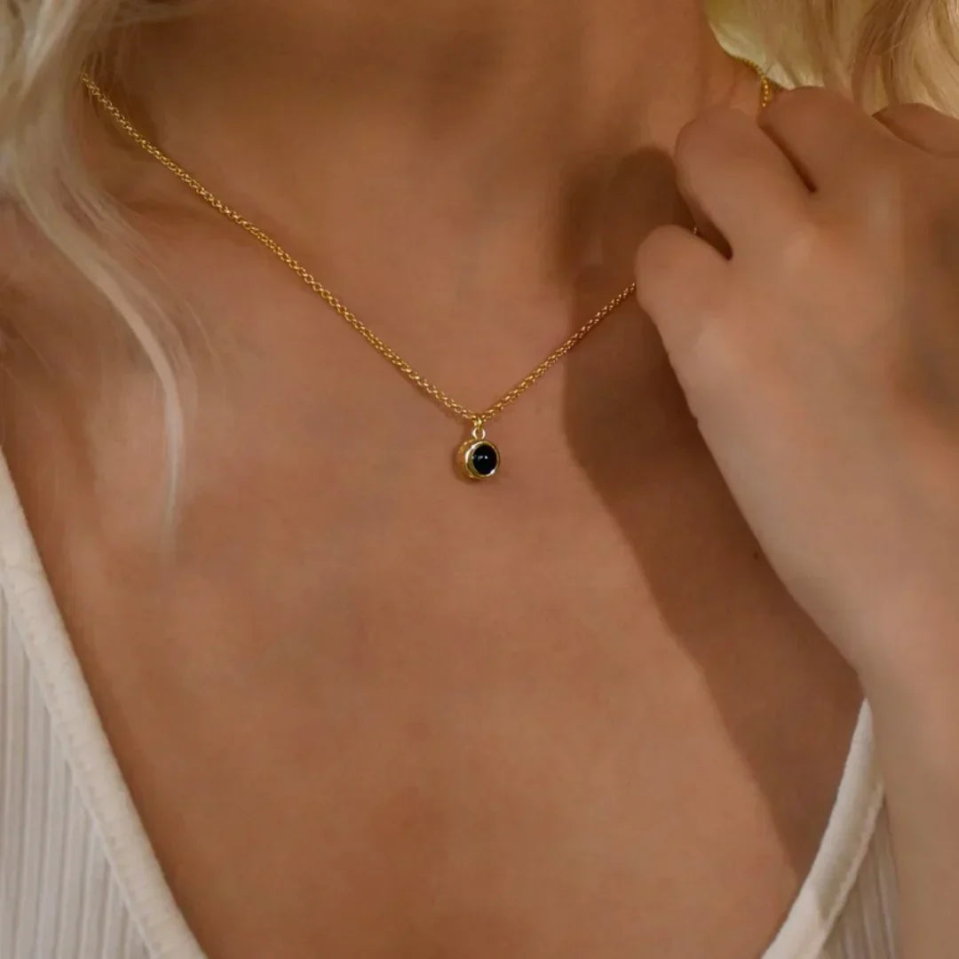 Woman in a white top touching the chain of a dainty gold photo projection necklace with a round stone