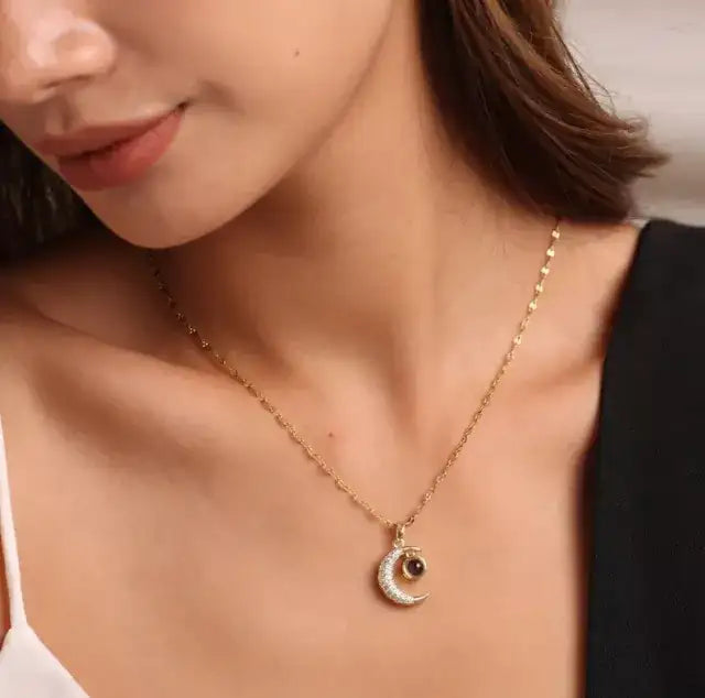 Woman in a black top wearing a gold moon pendant necklace with picture inside