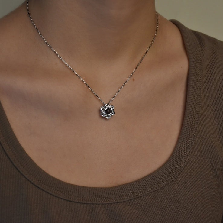 Close-up of a silver tone knot pendant necklace with picture inside worn with a brown scoop neck top