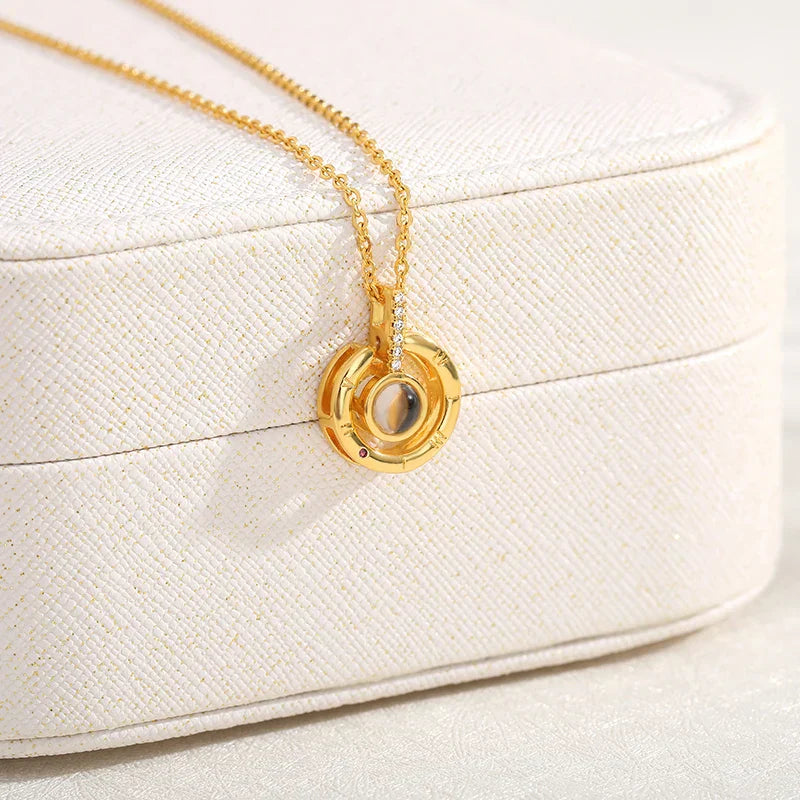 Gold necklace with picture inside, round double-ring pendant resting on a cream textured jewelry box