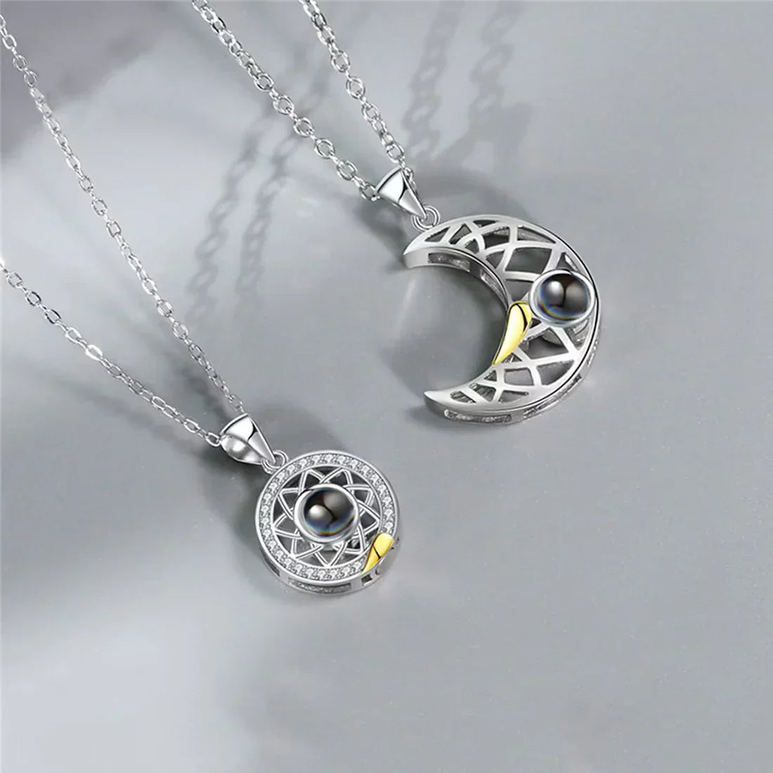 Matching sun and moon photo projection necklaces in silver tone with small gold hearts, on grey