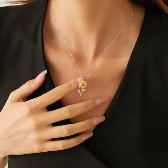 Woman in a black top touching her chest, wearing a small sunflower necklace with picture inside